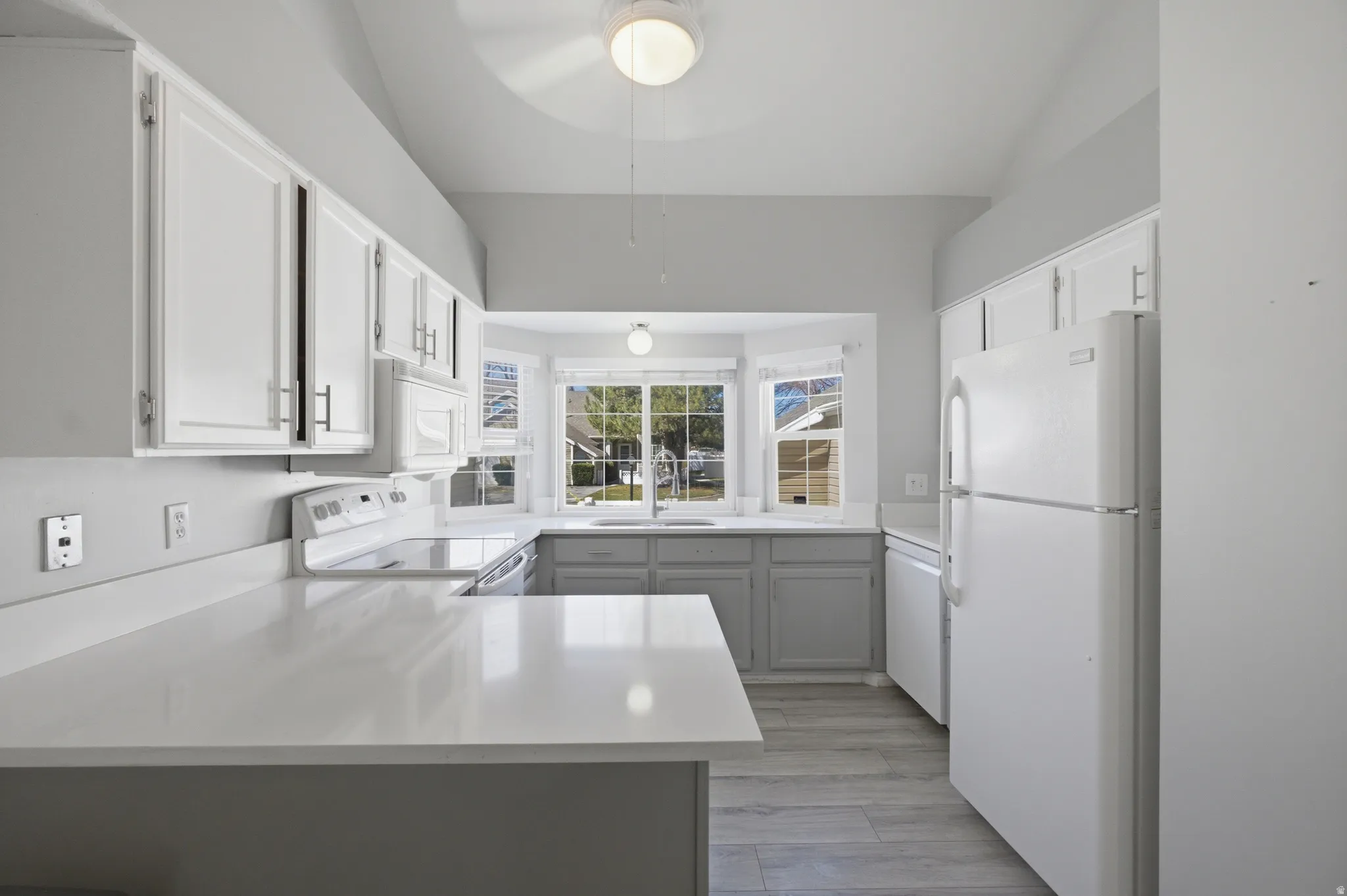 Kitchen with white appliances, light wood-style flooring, a peninsula, and white cabinetry