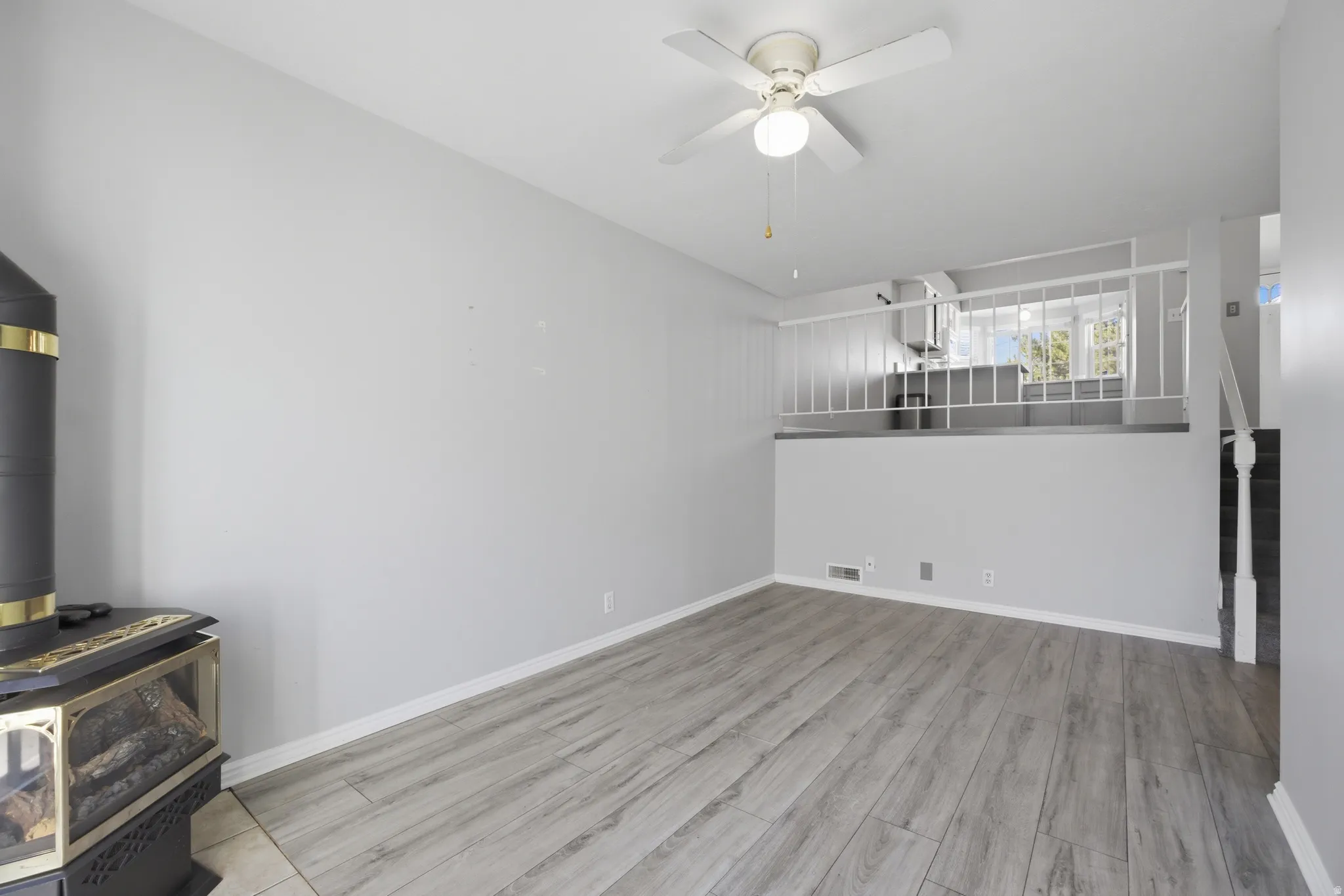 Unfurnished living room with ceiling fan, light wood finished floors, and a wood stove
