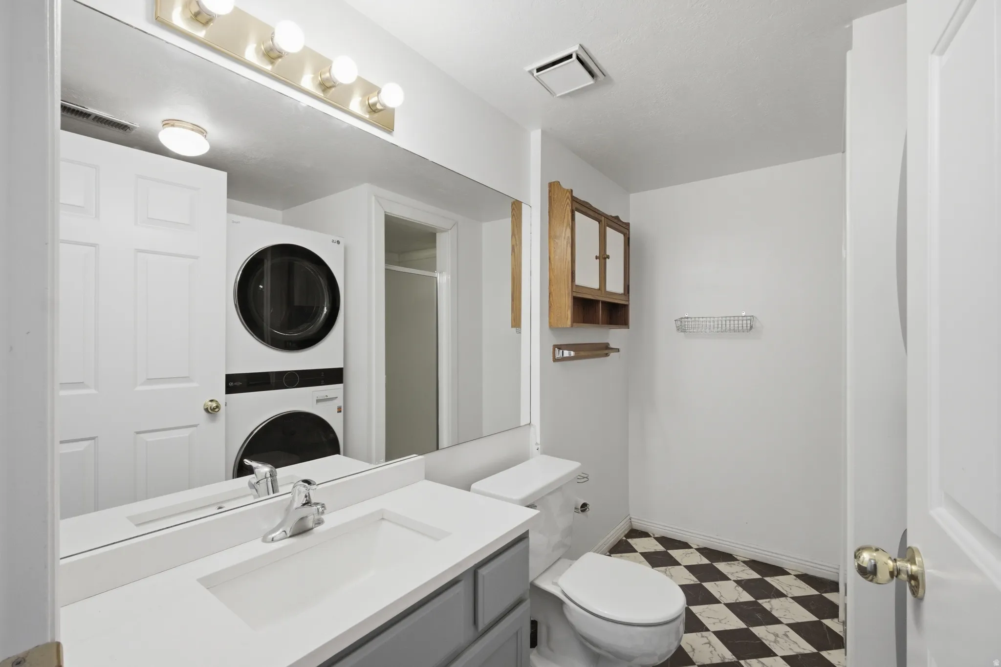 Bathroom featuring dark floors, vanity, stacked washer and clothes dryer, and a shower stall