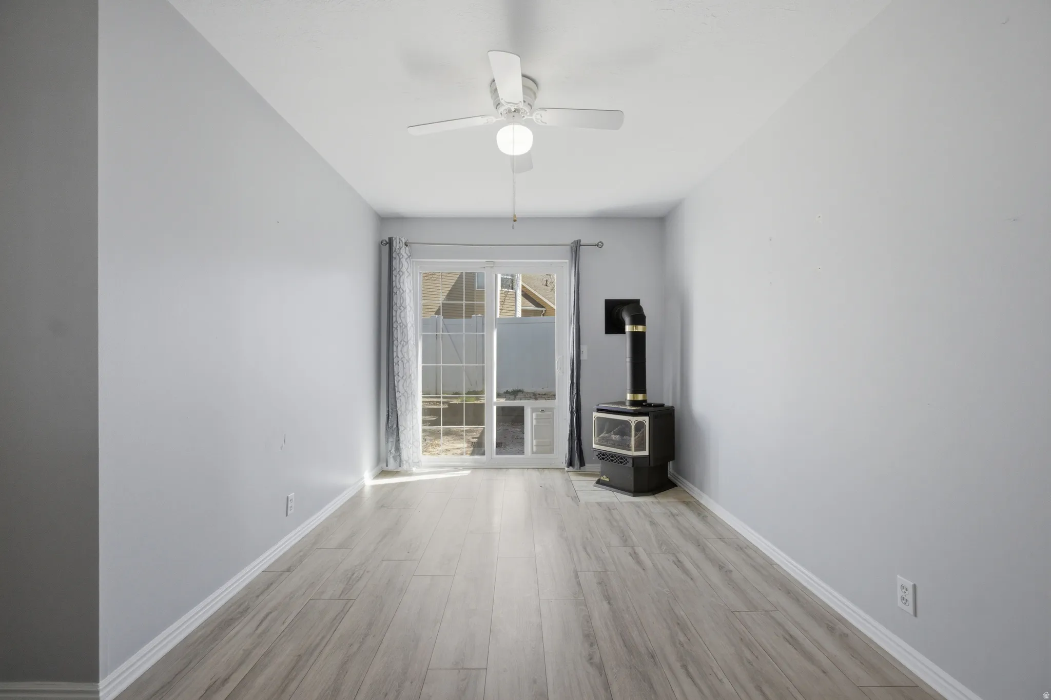 Spare room with light wood-style floors, a wood stove, and ceiling fan