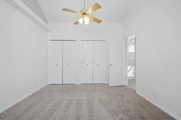 Unfurnished bedroom featuring multiple closets, vaulted ceiling, carpet floors, and ceiling fan