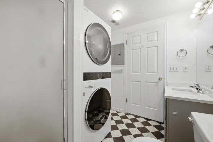 Laundry area with dark flooring, stacked washer and clothes dryer, and electric panel