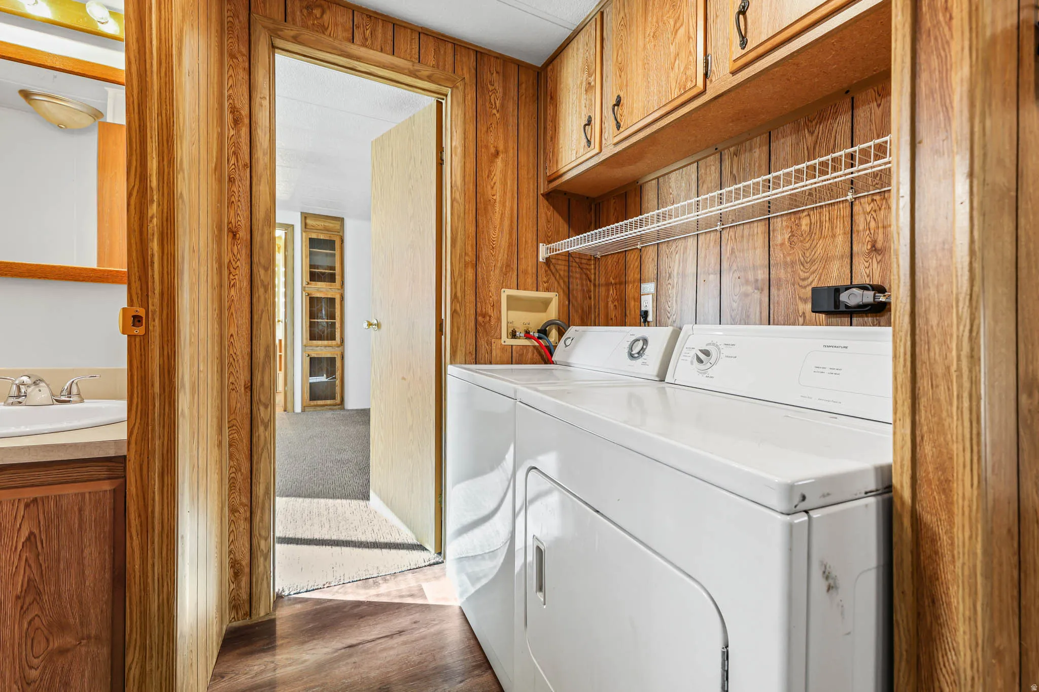 Laundry room featuring wooden walls, cabinet space, washer and dryer, and dark wood finished floors