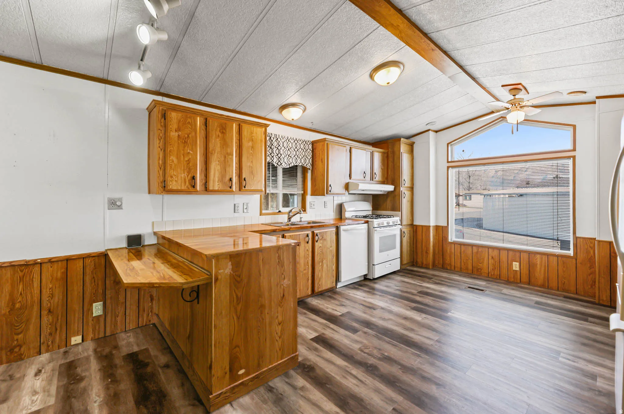 Kitchen featuring wooden walls, wainscoting, brown cabinetry, dark wood-style floors, and a peninsula