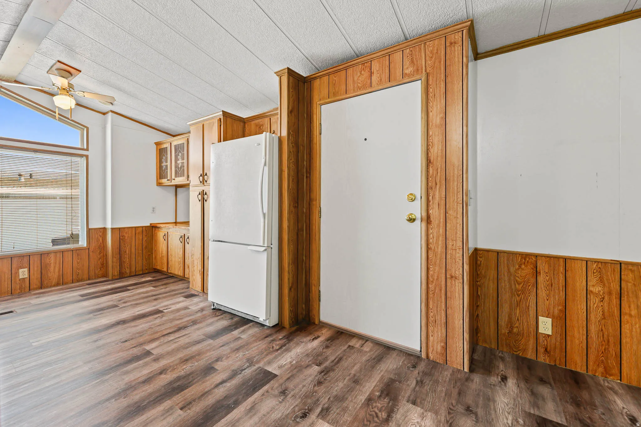 Kitchen with wood walls, a wainscoted wall, freestanding refrigerator, vaulted ceiling, and dark wood-type flooring
