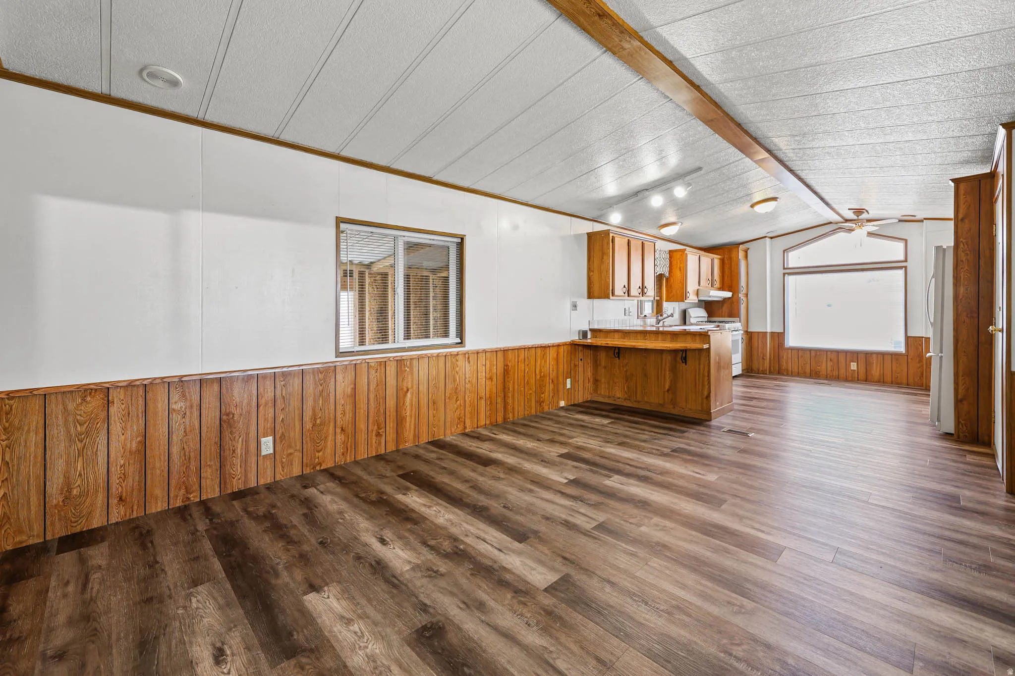 Unfurnished living room with wooden walls, dark wood finished floors, a wainscoted wall, a ceiling fan, and ornamental molding