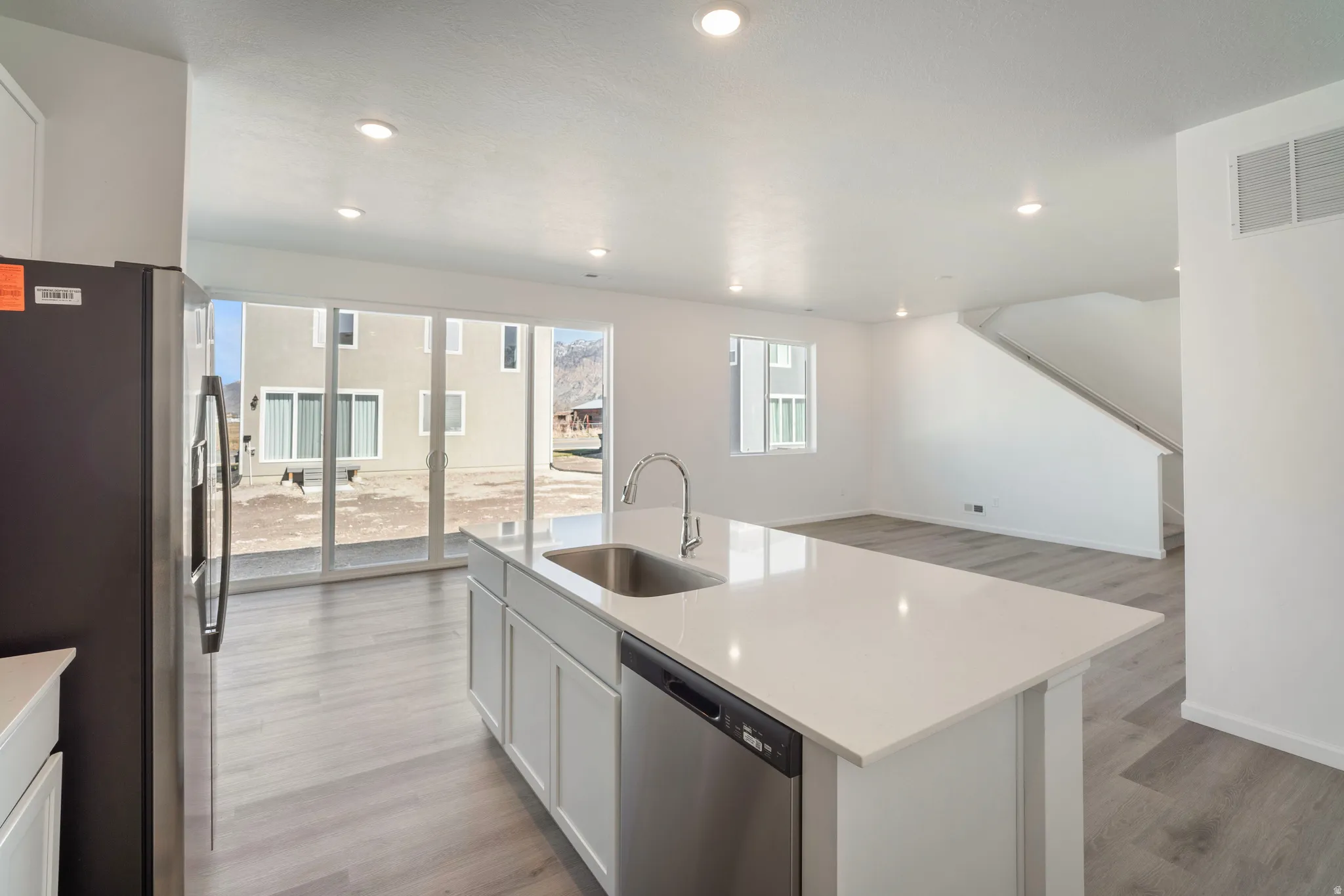 Kitchen featuring stainless steel appliances, white cabinetry, a kitchen island with sink, light wood finished floors, and light stone countertops