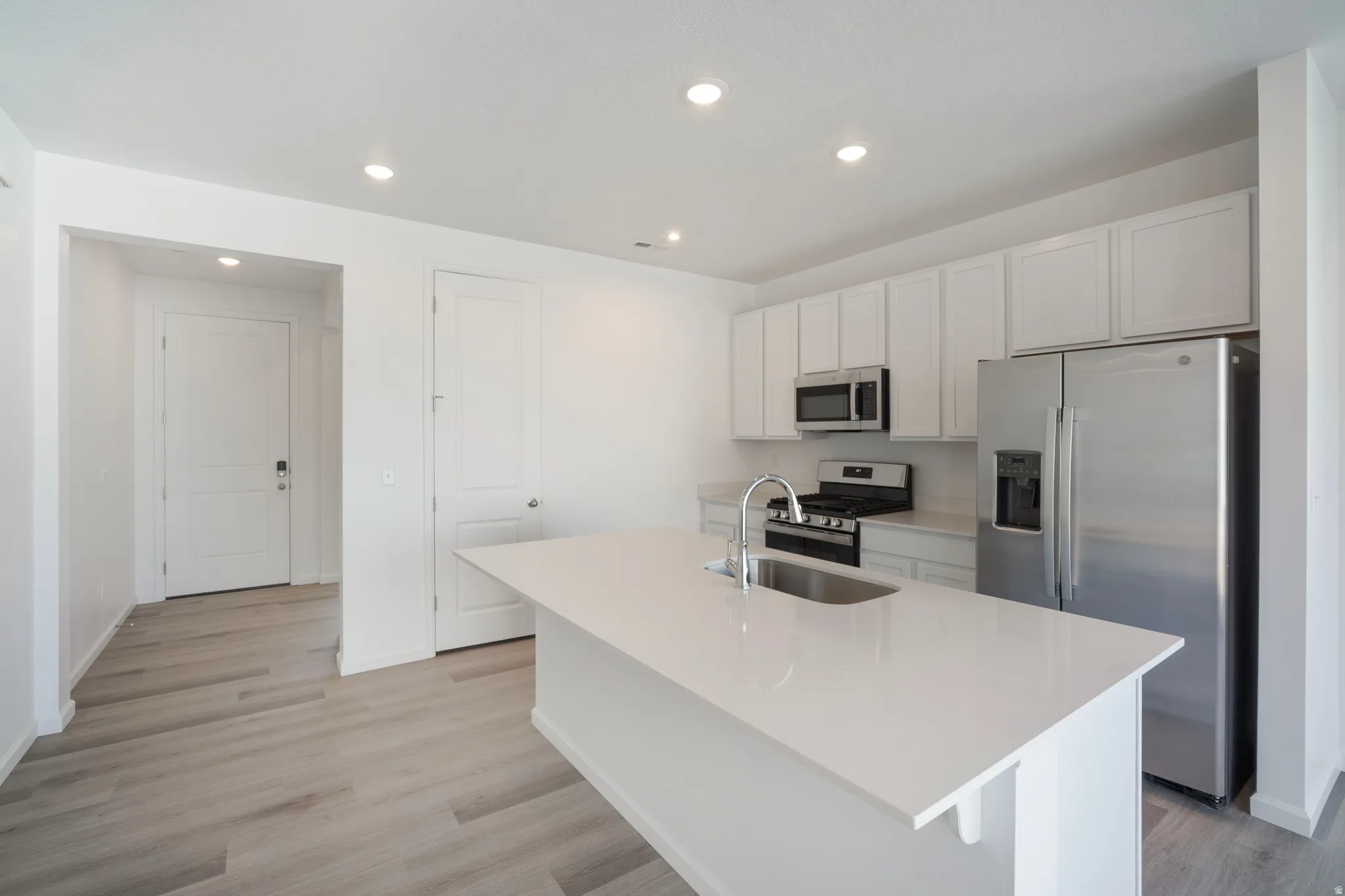 Kitchen featuring stainless steel appliances, white cabinetry, a kitchen island with sink, light wood-type flooring, and recessed lighting