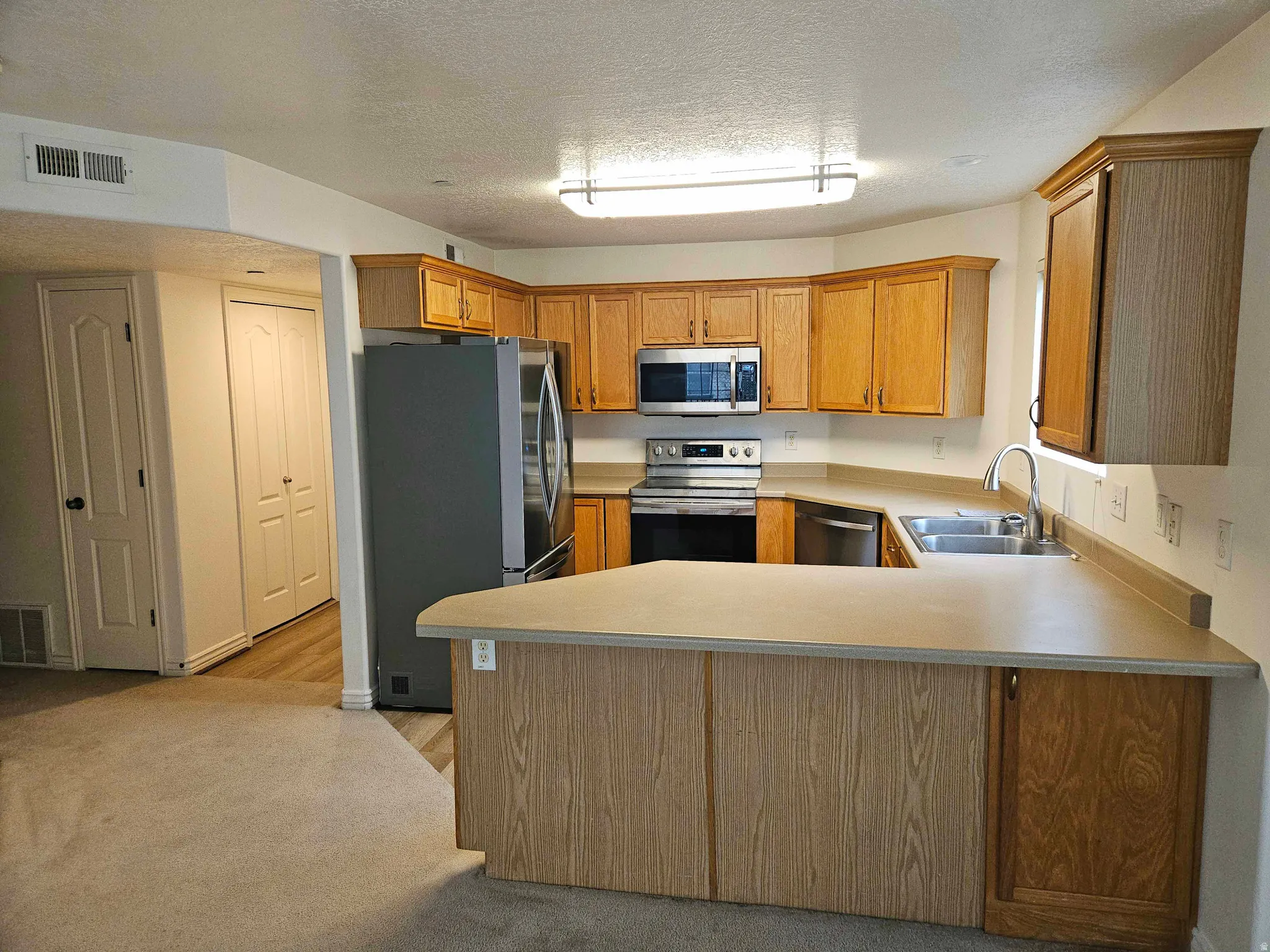 Kitchen featuring a peninsula, appliances with stainless steel finishes, light countertops, brown cabinets, and a textured ceiling