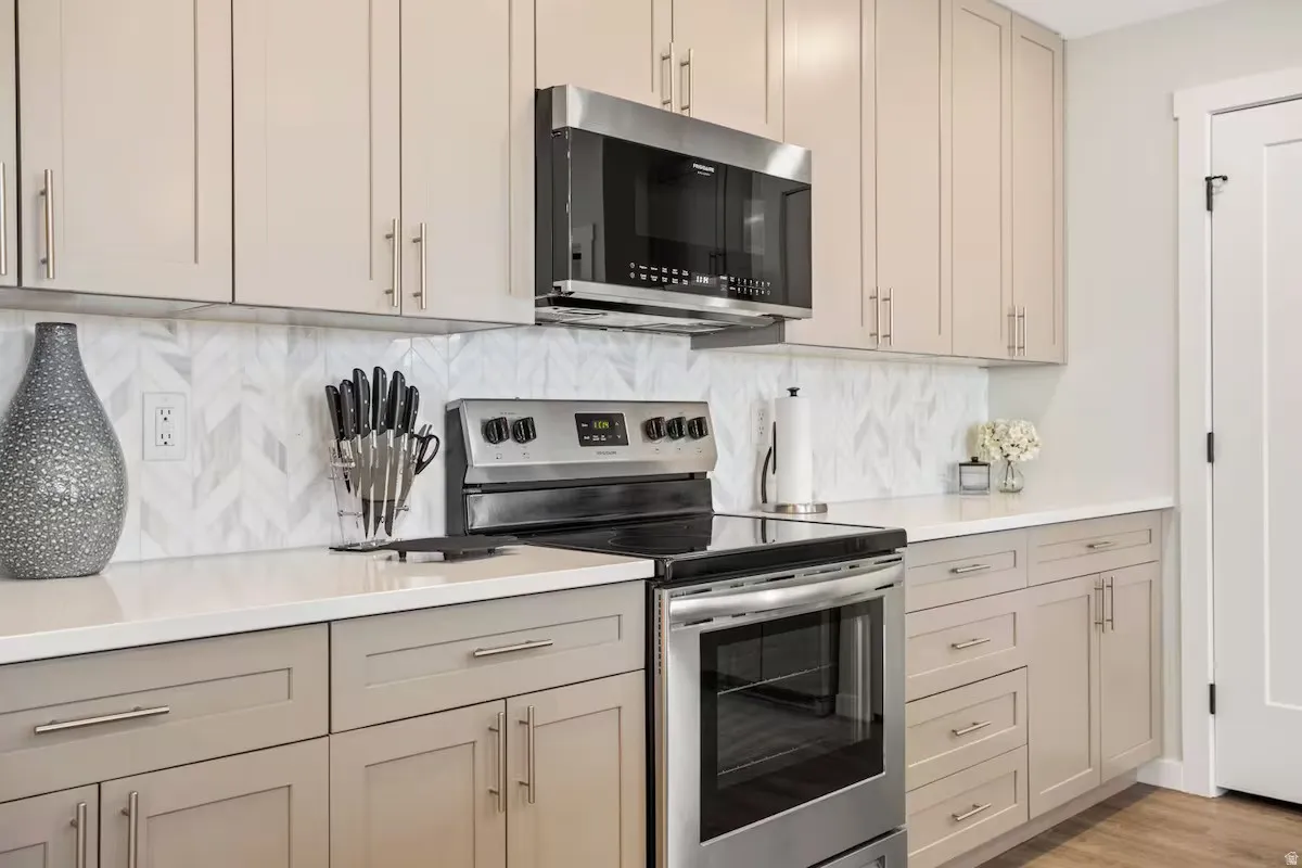 Kitchen featuring appliances with stainless steel finishes, light wood-type flooring, light stone counters, and tasteful backsplash
