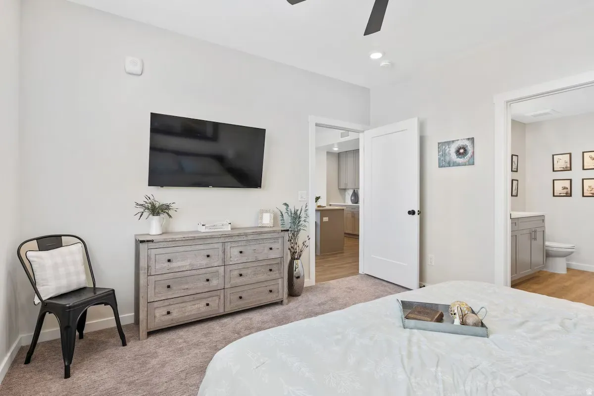 Bedroom with light colored carpet, a ceiling fan, and ensuite bathroom
