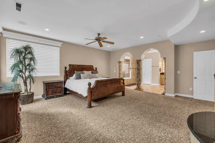 Bedroom with light colored carpet, arched walkways, recessed lighting, and a ceiling fan