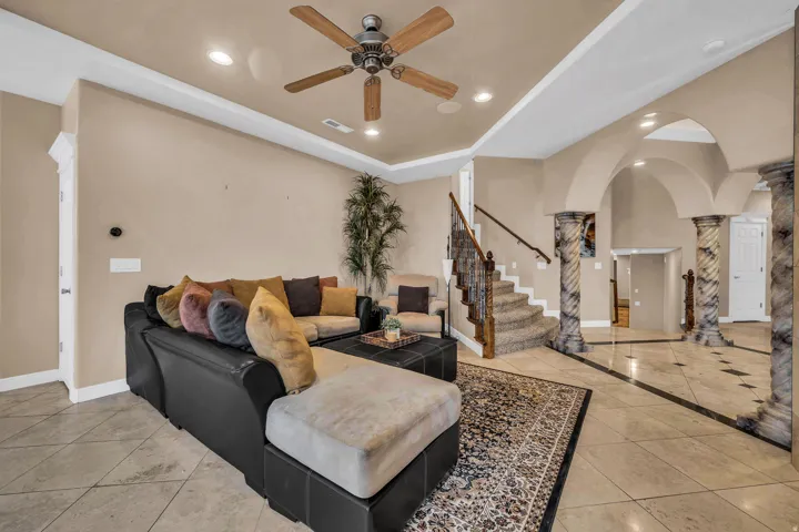 Living room with arched walkways, recessed lighting, decorative columns, inlaid floor details, and stairs
