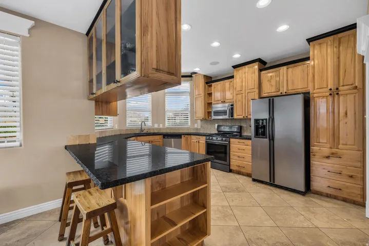 Kitchen featuring open shelves, stainless steel appliances, dark stone countertops, a kitchen breakfast bar, and light tile patterned floors