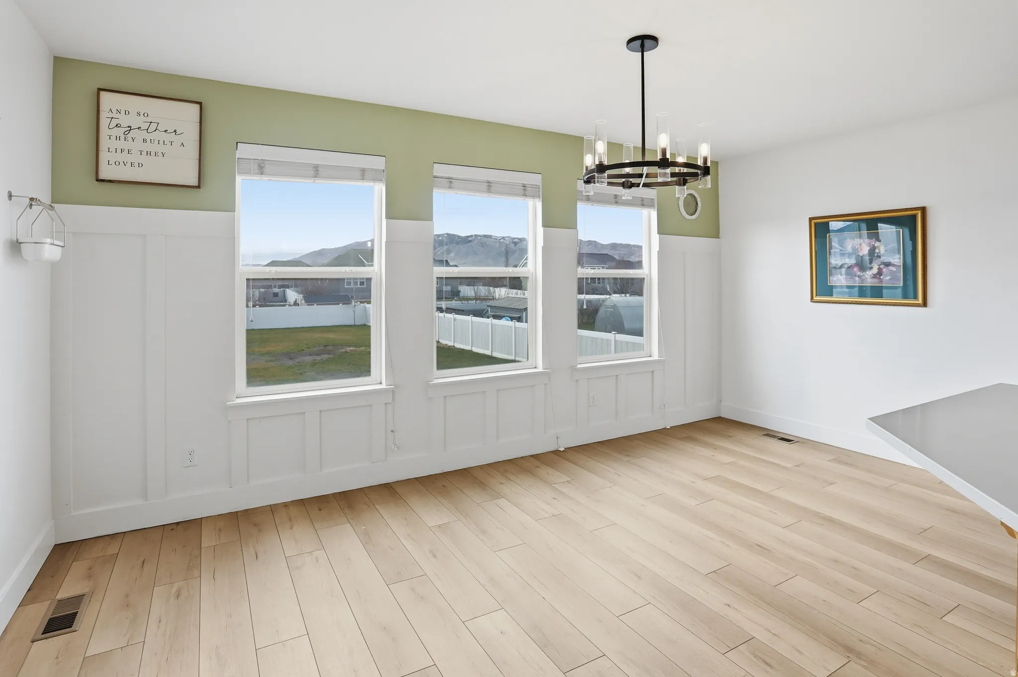 Unfurnished dining area with light wood finished floors, a chandelier, a mountain view, wainscoting, and a decorative wall