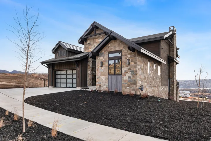 View of front of home with concrete driveway, a mountain view, stone siding, a metal roof, and a standing seam roof