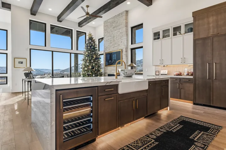 Kitchen with dark brown cabinetry, wine cooler, light stone counters, white cabinets, and tasteful backsplash