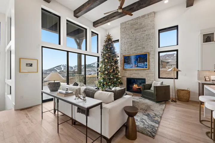 Living area featuring light wood-style flooring, healthy amount of natural light, a large fireplace, a high ceiling, and ceiling fan