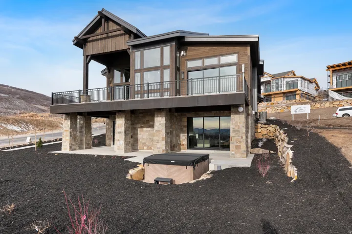 Rear view of property with stone siding, a hot tub, a balcony, and a patio area