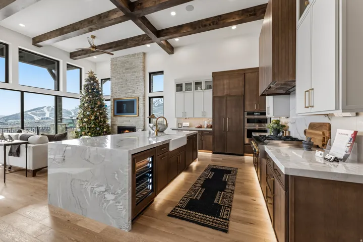 Kitchen featuring dark brown cabinets, light stone countertops, glass insert cabinets, beam ceiling, and a high ceiling