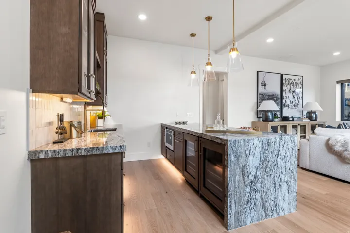 Kitchen featuring dark brown cabinets, a peninsula, light stone counters, light wood-type flooring, and decorative light fixtures