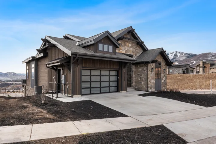 View of front facade with a mountain view, stone siding, concrete driveway, a garage, and roof with shingles