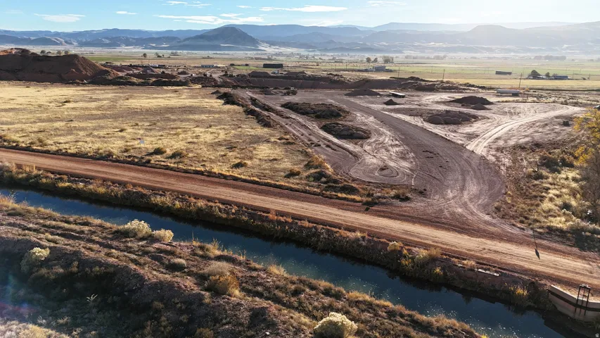 Expansive land parcel featuring open terrain, a dirt road, and a water channel