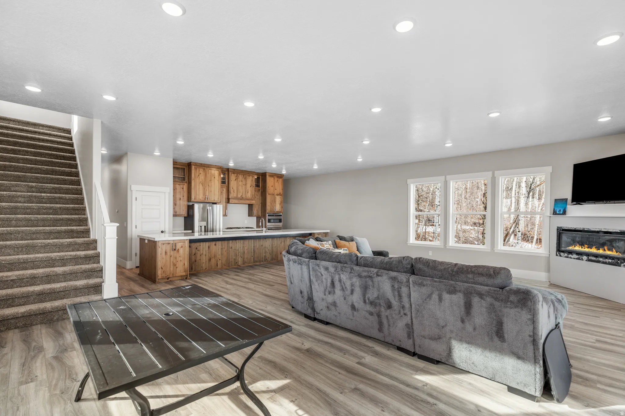 Living room with stairs, light wood finished floors, recessed lighting, and a glass covered fireplace