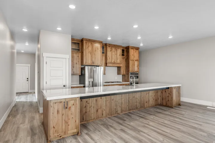 Kitchen with recessed lighting, stainless steel appliances, a large island with sink, light wood-style flooring, and light stone counters