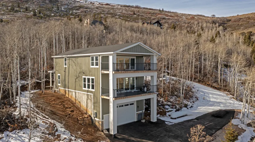 Snow covered back of property with a balcony and an attached garage