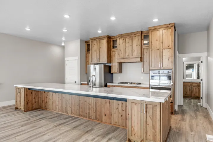 Kitchen featuring light stone countertops, light wood-style floors, glass insert cabinets, recessed lighting, and stainless steel appliances