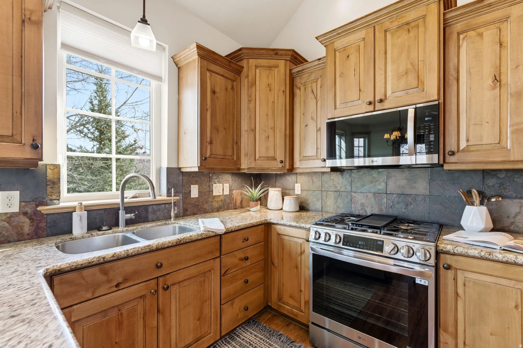 Kitchen with appliances with stainless steel finishes, light stone countertops, backsplash, and vaulted ceiling