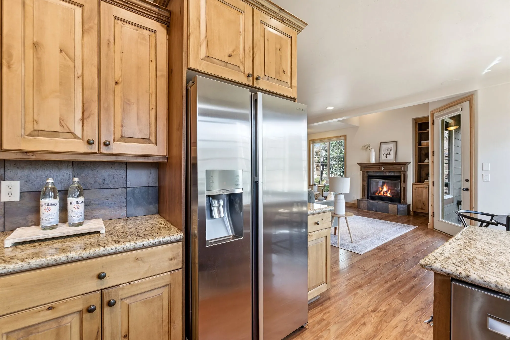 Kitchen featuring stainless steel appliances, light stone counters, a glass covered fireplace, light wood-style floors, and built in features