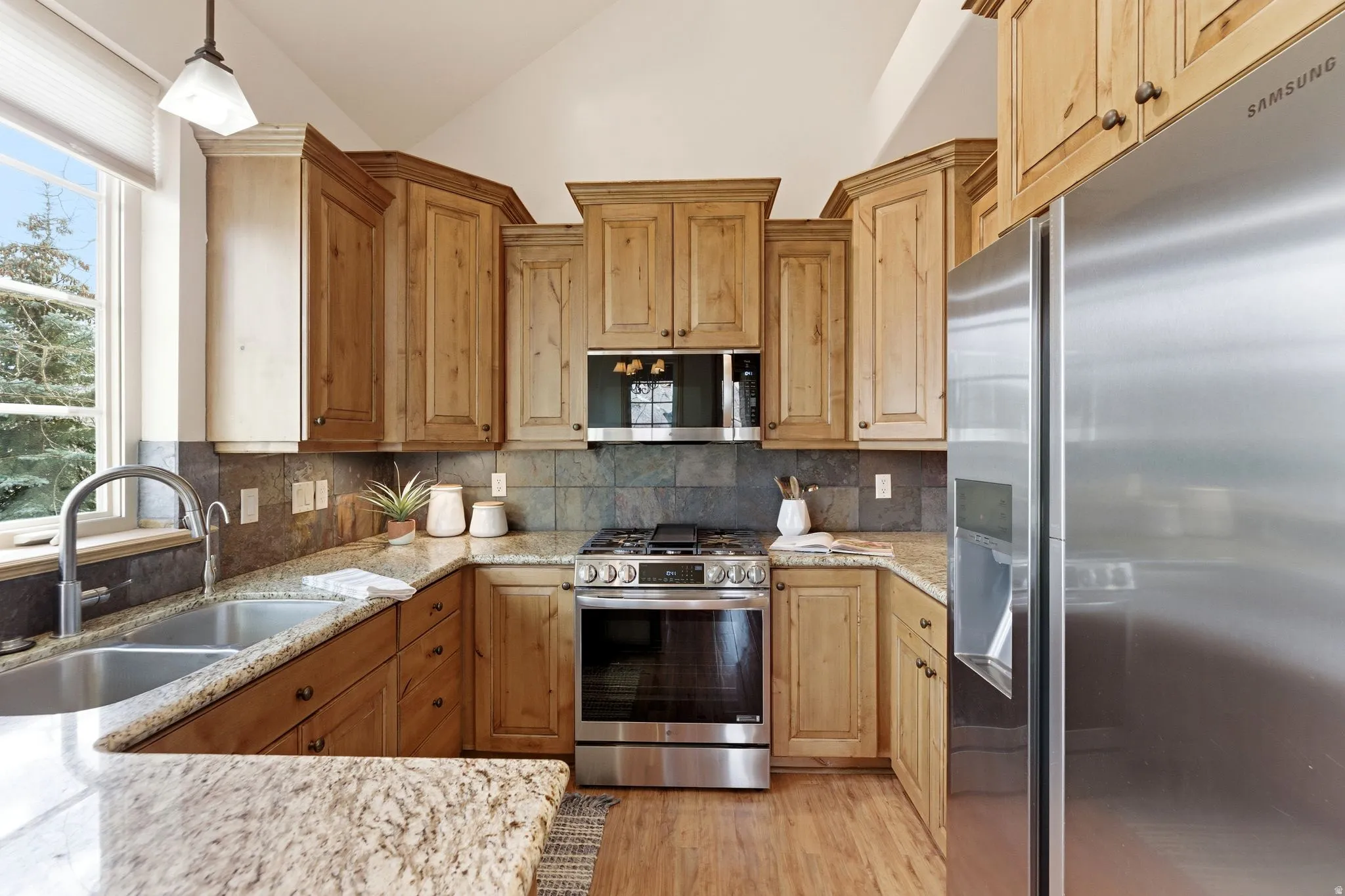 Kitchen with stainless steel appliances, plenty of natural light, vaulted ceiling, light stone countertops, and hanging light fixtures