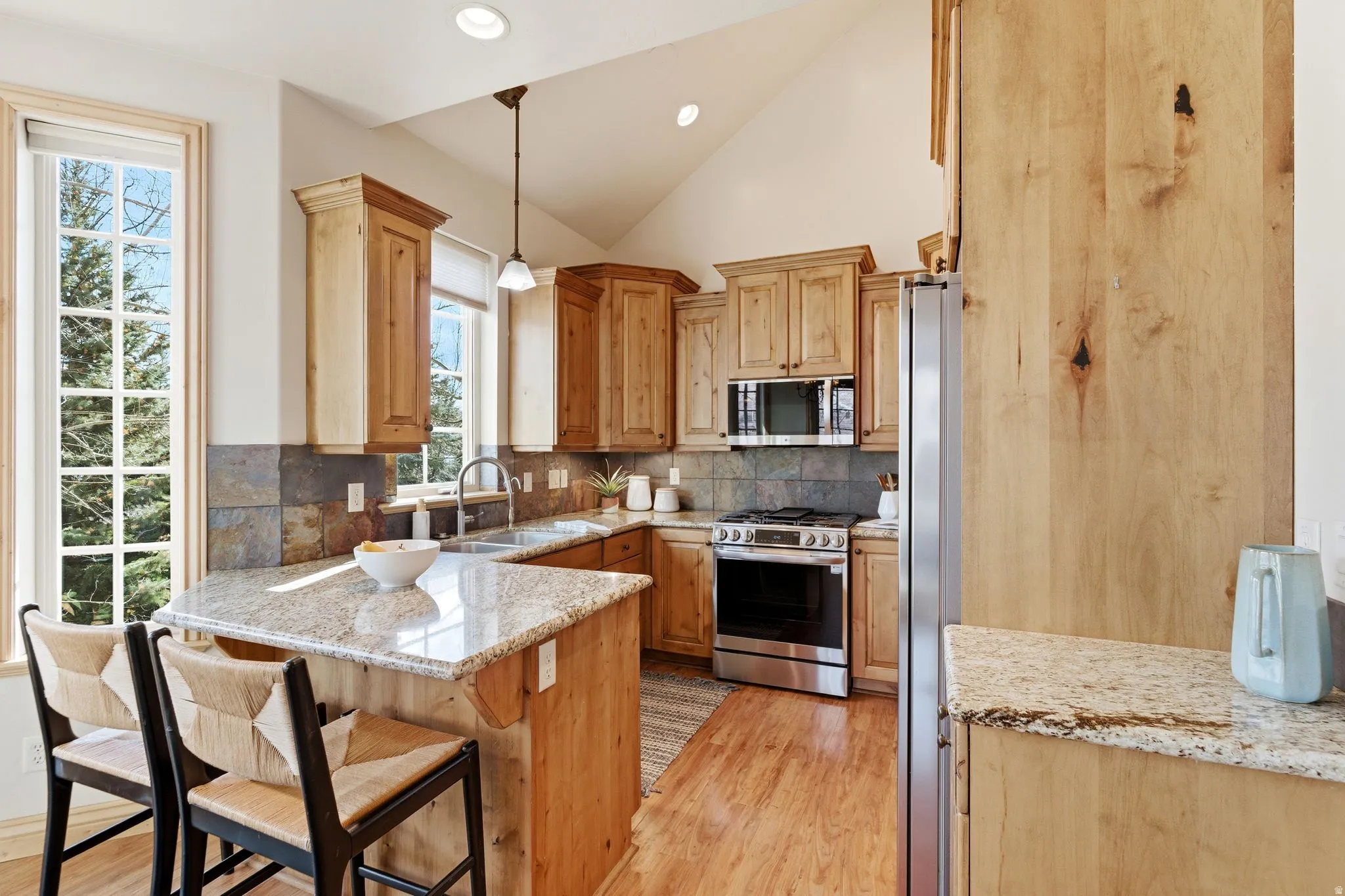 Kitchen featuring light stone counters, pendant lighting, appliances with stainless steel finishes, light wood-style flooring, and decorative backsplash
