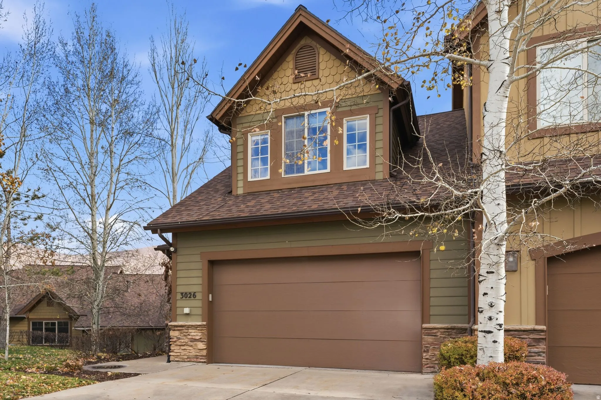 View of front of house featuring stone siding, roof with shingles, an attached garage, and driveway
