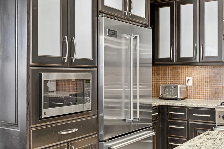 Kitchen with glass insert cabinets, appliances with stainless steel finishes, light stone counters, and tasteful backsplash