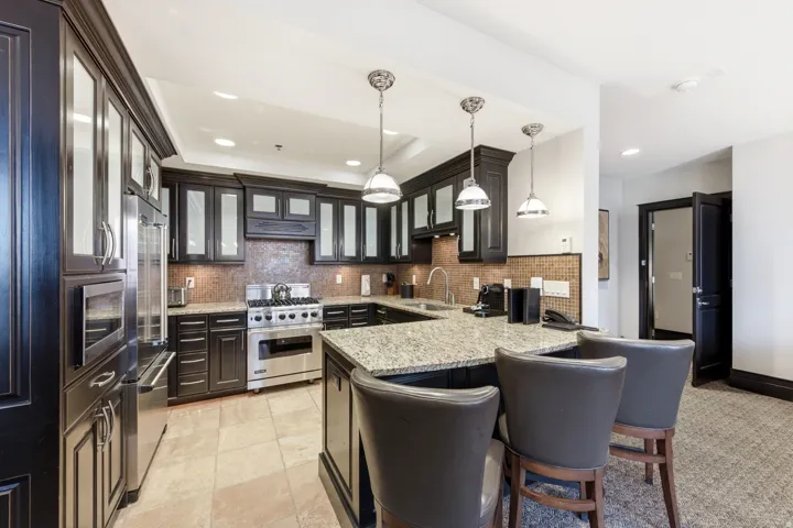 Kitchen featuring decorative light fixtures, a kitchen bar, high end appliances, light stone counters, and glass insert cabinets
