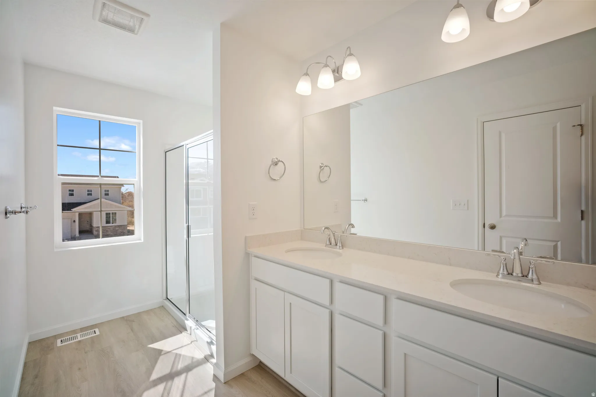 Bathroom with double vanity, a stall shower, and light wood-style floors