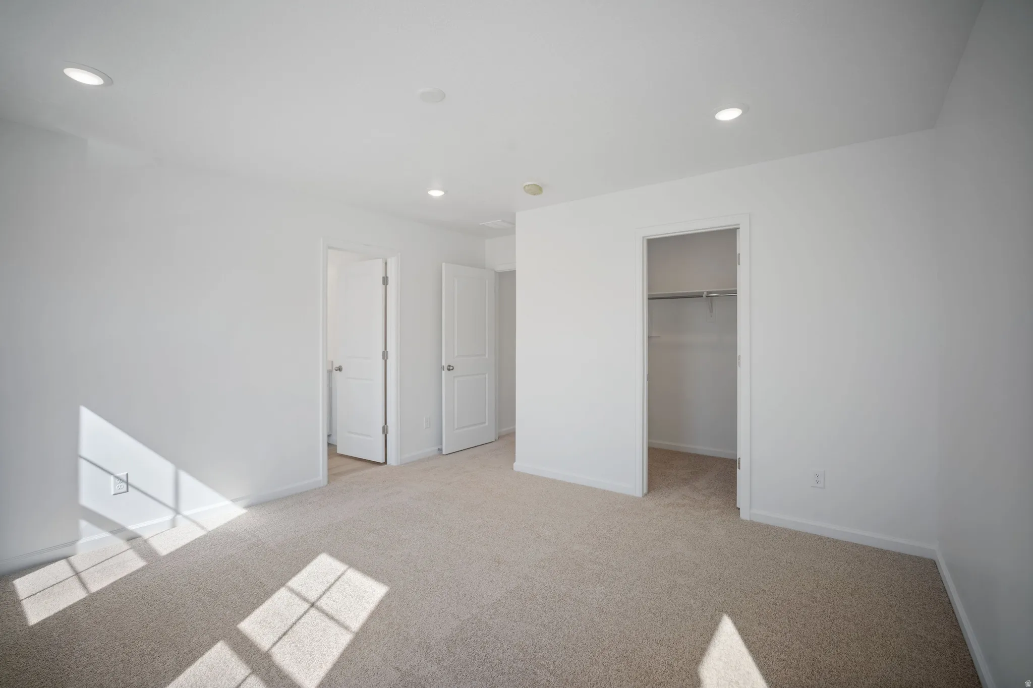 Unfurnished bedroom with a spacious closet, light carpet, and recessed lighting