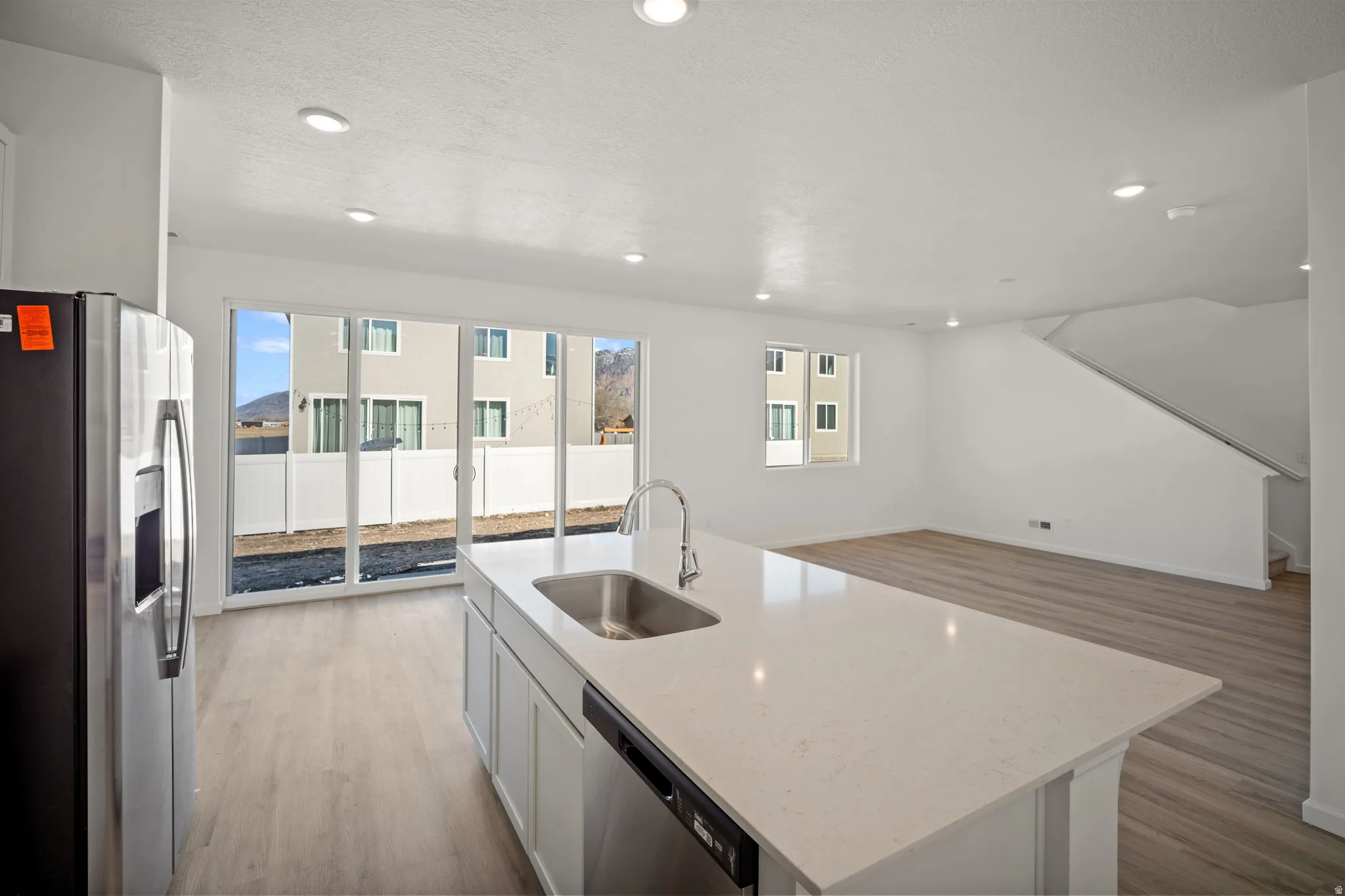 Kitchen featuring stainless steel appliances, a center island with sink, light stone countertops, open floor plan, and light wood-type flooring