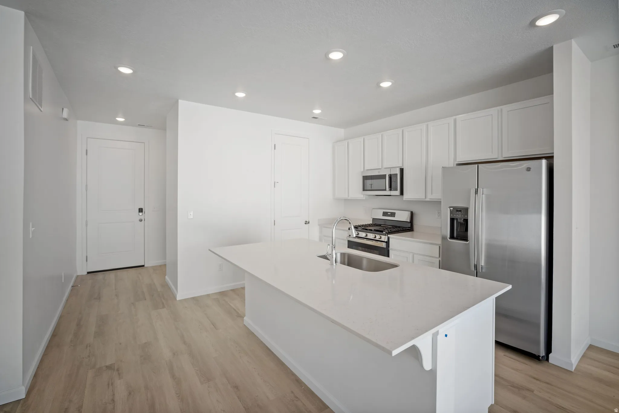 Kitchen featuring stainless steel appliances, white cabinetry, recessed lighting, light stone counters, and light wood-type flooring