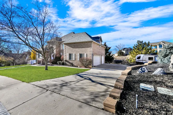 View of side of property featuring concrete driveway, brick siding, a lawn, a residential view, and an attached garage