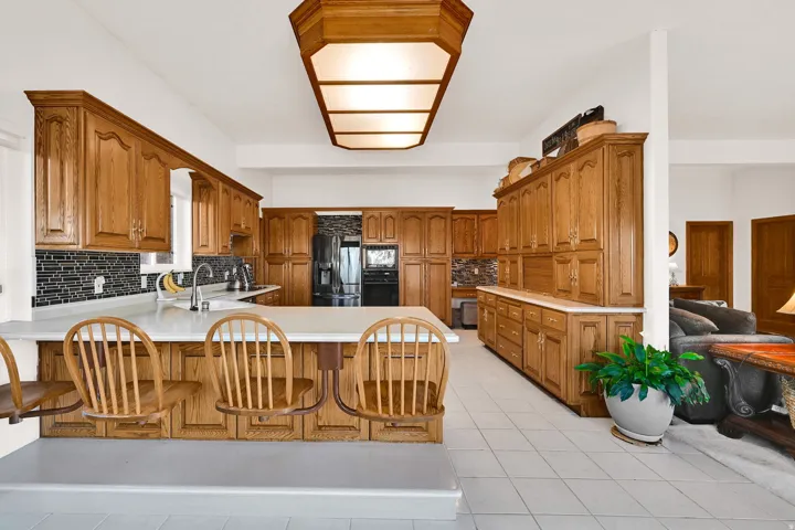 Kitchen with brown cabinetry, light countertops, a peninsula, and backsplash
