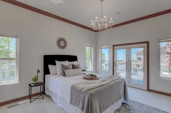 Carpeted bedroom featuring multiple windows, access to outside, a chandelier, and crown molding