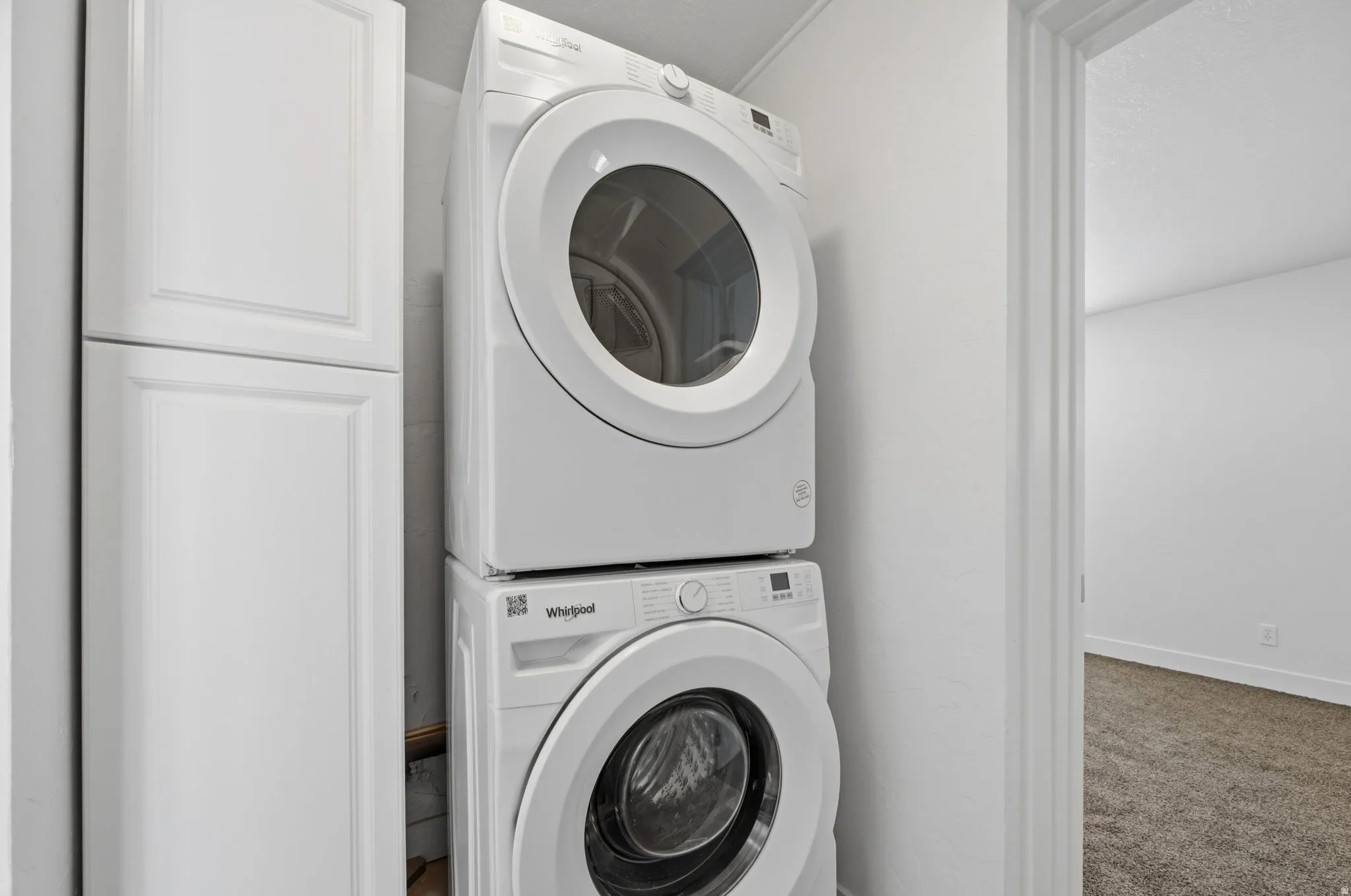 Laundry area with stacked washing machine and dryer, carpet floors, and cabinet space