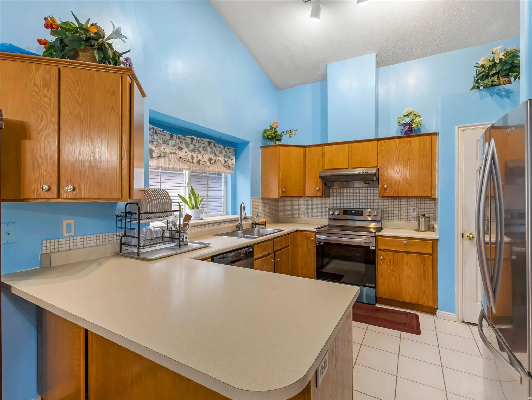Kitchen featuring brown cabinets, stainless steel appliances, a peninsula, light countertops, and light tile patterned floors