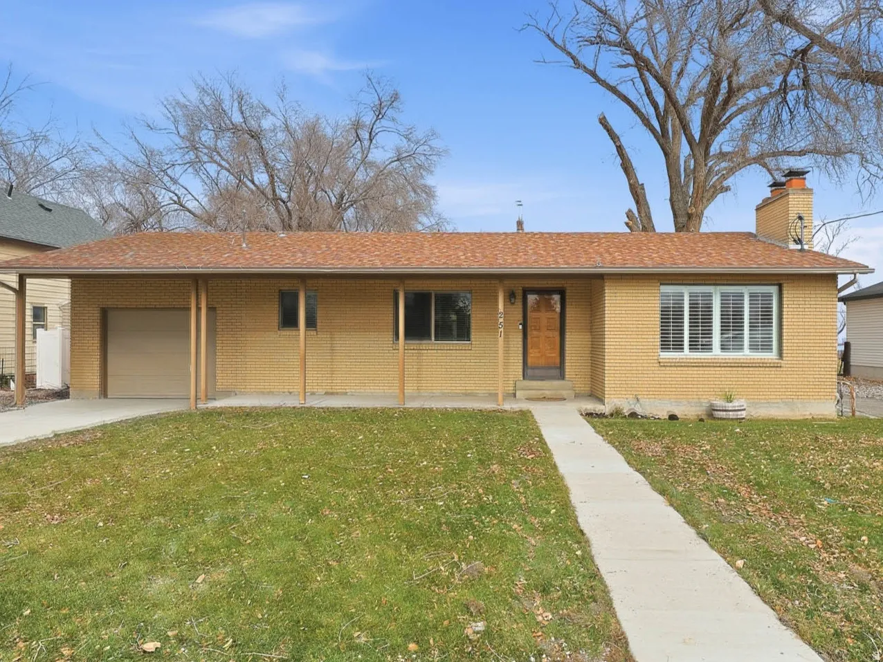 Ranch-style house featuring a front yard, brick siding, a chimney, concrete driveway, and an attached garage