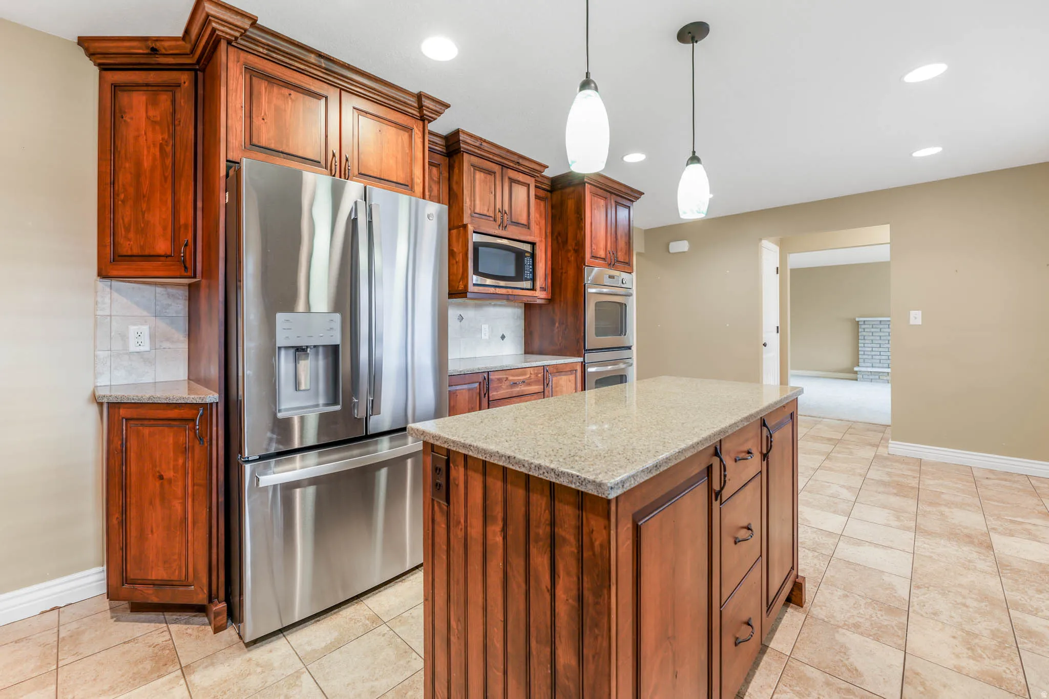 Kitchen featuring appliances with stainless steel finishes, light stone counters, backsplash, pendant lighting, and a center island