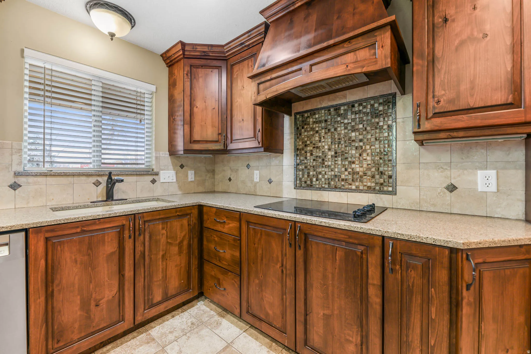 Kitchen featuring custom range hood, light stone countertops, stainless steel dishwasher, black electric stovetop, and tasteful backsplash